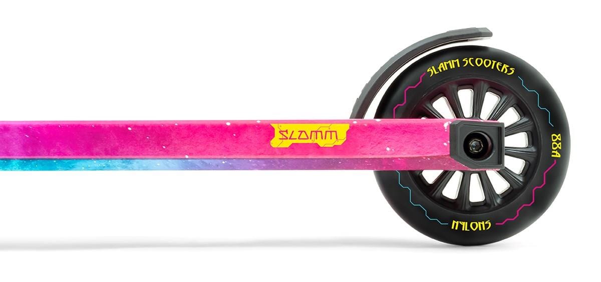 A close-up of the Slamm Mischief Complete Stunt Scooter - Nebula highlights its vivid Nebula Wrap on the deck, fusing shades of pink, purple, and blue with a prominent yellow Slamm logo. The 110mm wheels come in black with white text featuring "SLAMM SCOOTERS" and "NYLONS.