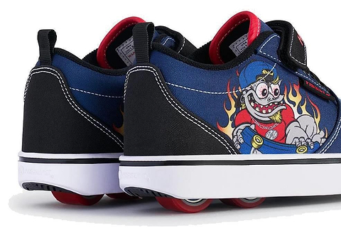 A close-up of two Heelys Pro 20 Prints X2 Boys Shoes in navy and red by Heelys, featuring wheels in the soles, red interiors, and a cartoon character with wild eyes and flames on the sides.