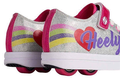 Close-up of Heelys Snazzy X2 Girls Shoes in silver with rainbow stripes and heart details. Features two pink wheels per shoe, pink wheels on the heels, and "Heelys" in purple on the side. Brand: Heelys.