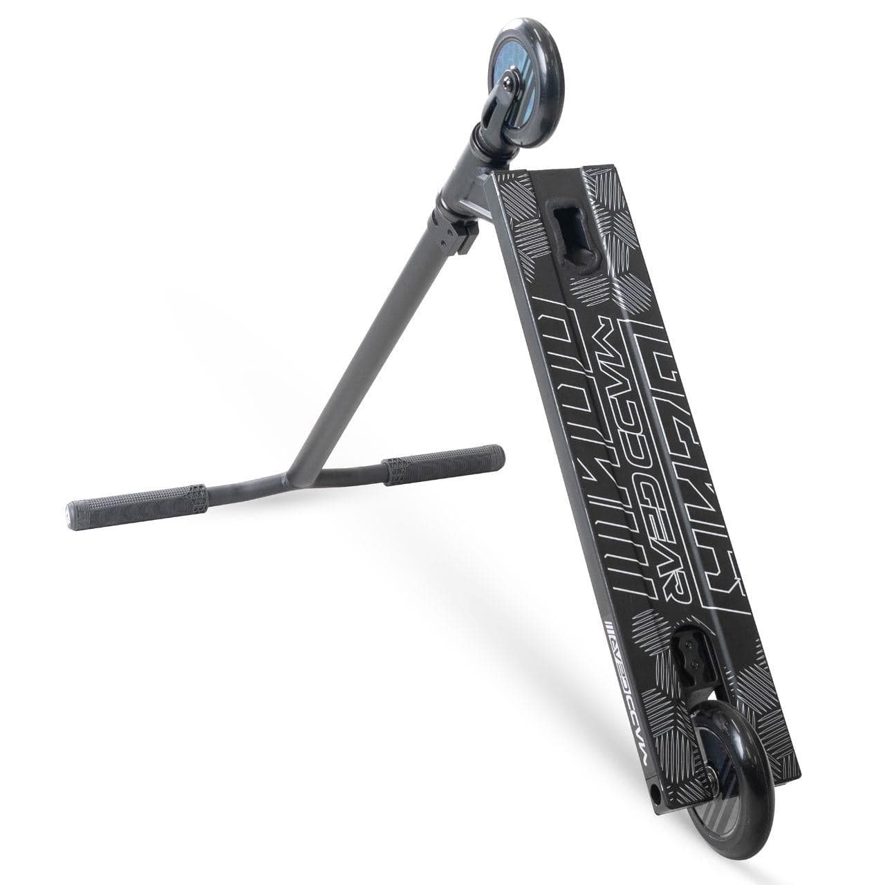 A Madd Gear MG 3 Zen Complete Stunt Scooter - Black / Black by MGP with a sturdy one-piece steel T-bar, grip tape, two small wheels, and bold "MAD GEAR" deck graphics is lying on its side.