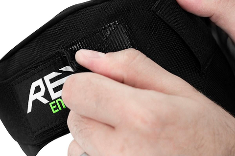 Close-up of hands adjusting the Velcro strap of a black sports or weightlifting belt, enhanced with REKD Energy foam for added comfort. The belt features striking black and white lettering.