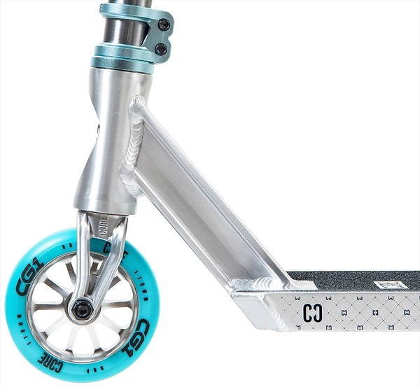 Close-up of the CORE CG1 Complete Stunt Scooter in Raw/Teal, featuring a turquoise "CG1"-labeled wheel, black grip deck with a geometric pattern, and metallic clamp and fork. Brand: CORE.
