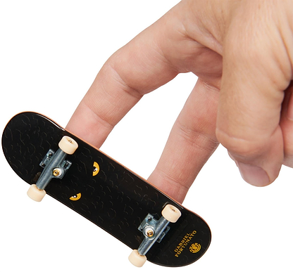 A hand uses two fingers to ride a Tech Deck M01 Deluxe 4 Pack Fingerboards - Element mini skateboard against a white background.