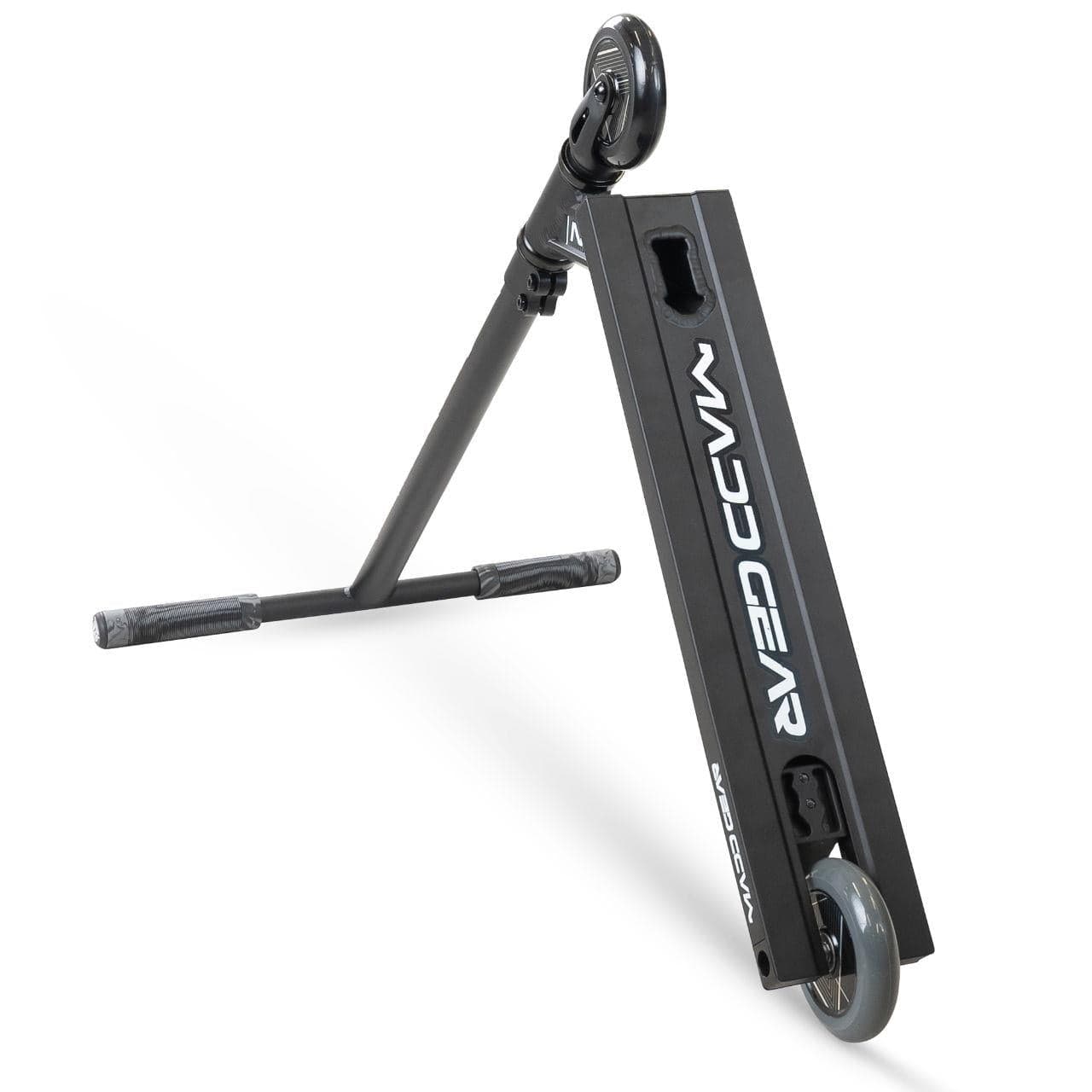 The Madd Gear MG 1 Raven Complete Stunt Scooter in black is shown on its side, highlighting the lightweight deck with the Madd Gear (MGP) logo in white, as well as the front wheel and handlebars.