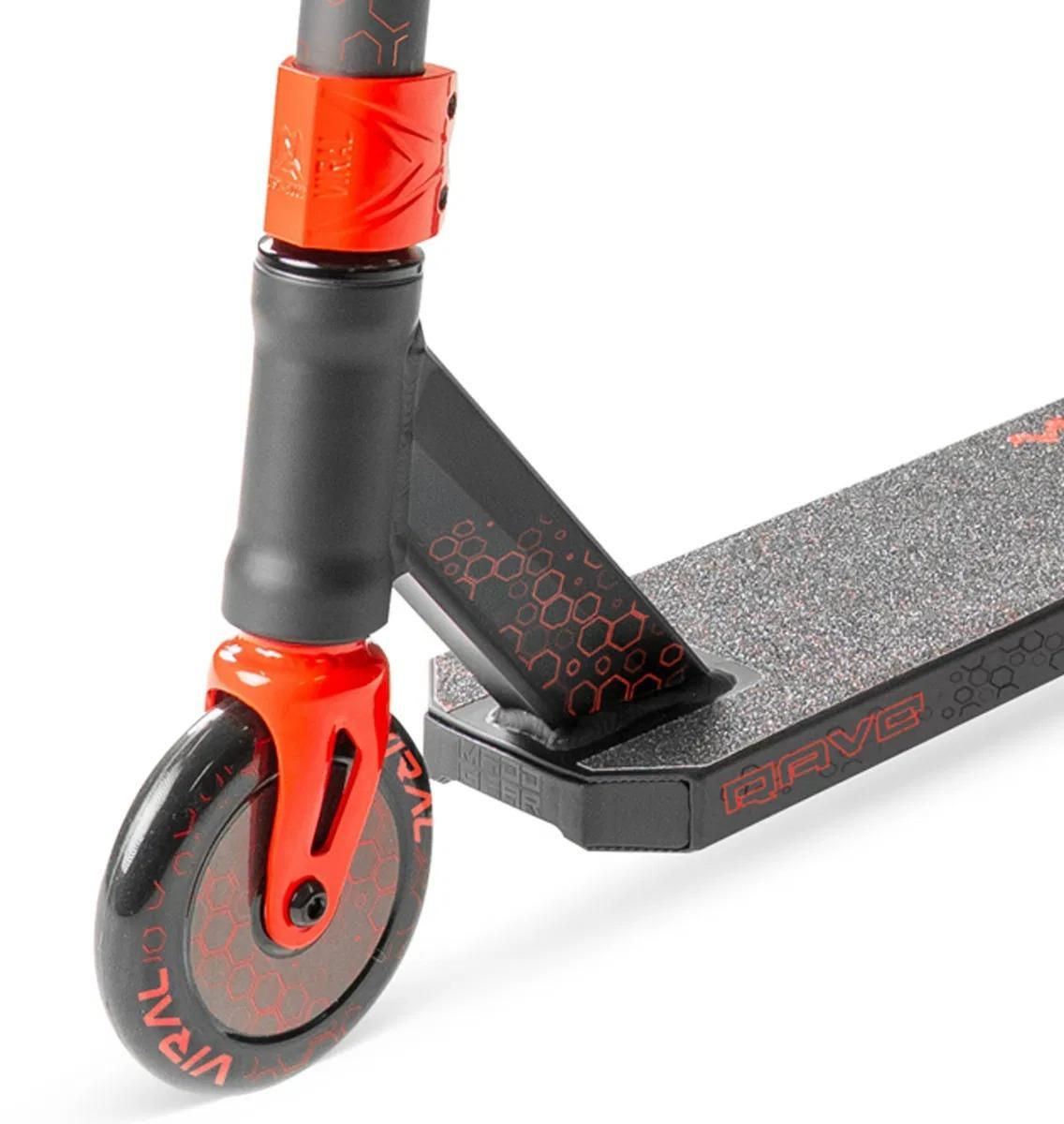 Close-up of the Madd Gear Viral Rave Complete Stunt Scooter - Inferno by MGP, featuring a black and red front wheel, fork, and deck with grip tape and honeycomb details. The deck displays the word "BRAVE" in bold red accents.