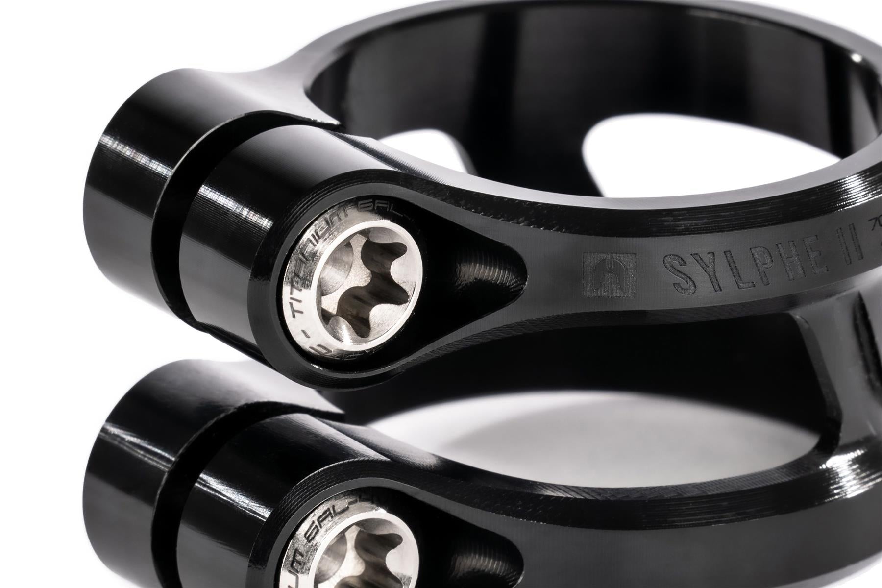 Close-up of two stacked Ethic DTC Sylphe V2 2 Bolt Oversized Stunt Scooter Clamps in black, featuring engraved Ethic branding, hex bolts, and a curved, lightweight design that showcases their sleek finish and precise construction.
