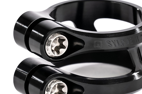 Close-up of two stacked Ethic DTC Sylphe V2 2 Bolt Oversized Stunt Scooter Clamps in black, featuring engraved Ethic branding, hex bolts, and a curved, lightweight design that showcases their sleek finish and precise construction.