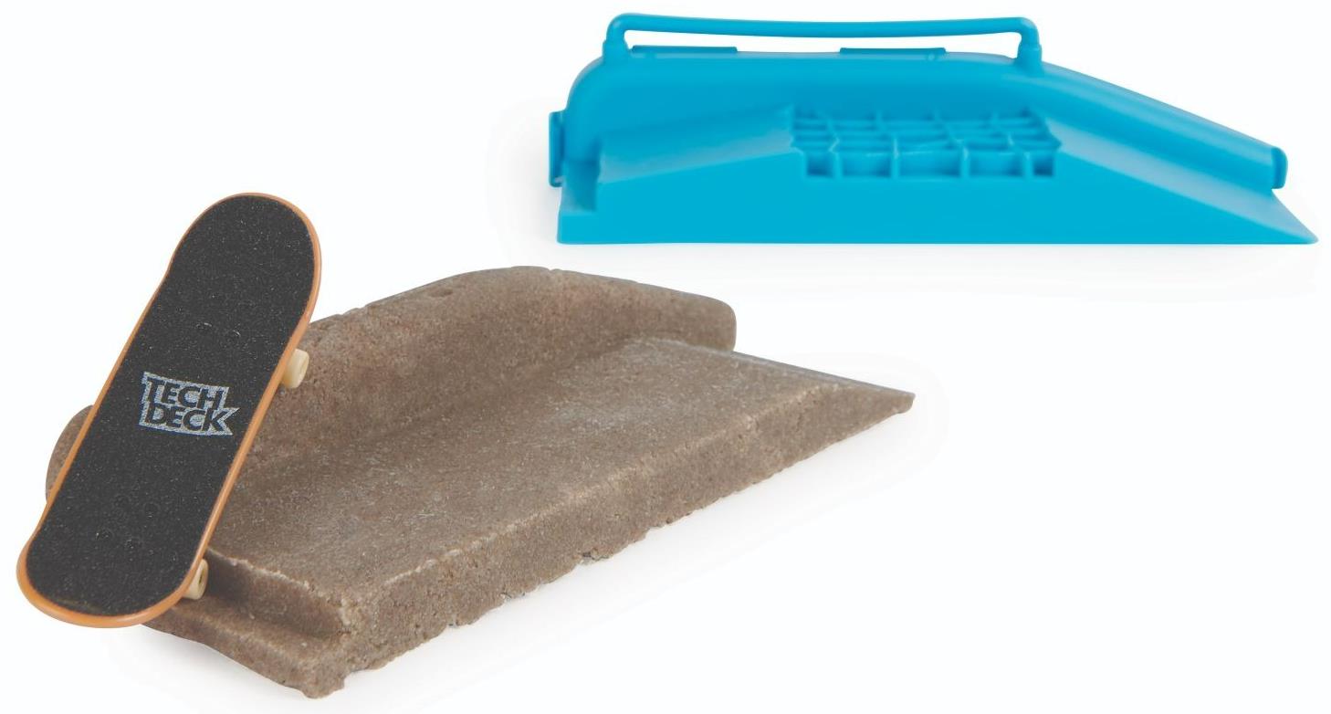 A miniature Tech Deck fingerboard is set on a ledge from the Tech Deck DIY Concrete Reusable Fingerboard Ramp Modelling Set, with a blue plastic skate ramp and reusable concrete compound in the background.