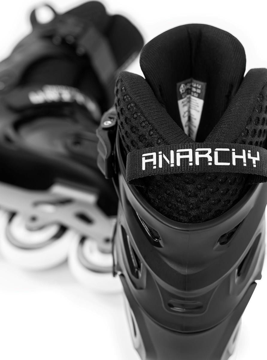 Close-up of Anarchy Unity Adjustable Inline Skates - Black, displaying "ANARCHY" on the back strap. They feature a durable plastic and aluminum frame, white wheels, and can adjust to four sizes, all set against a pristine white background.