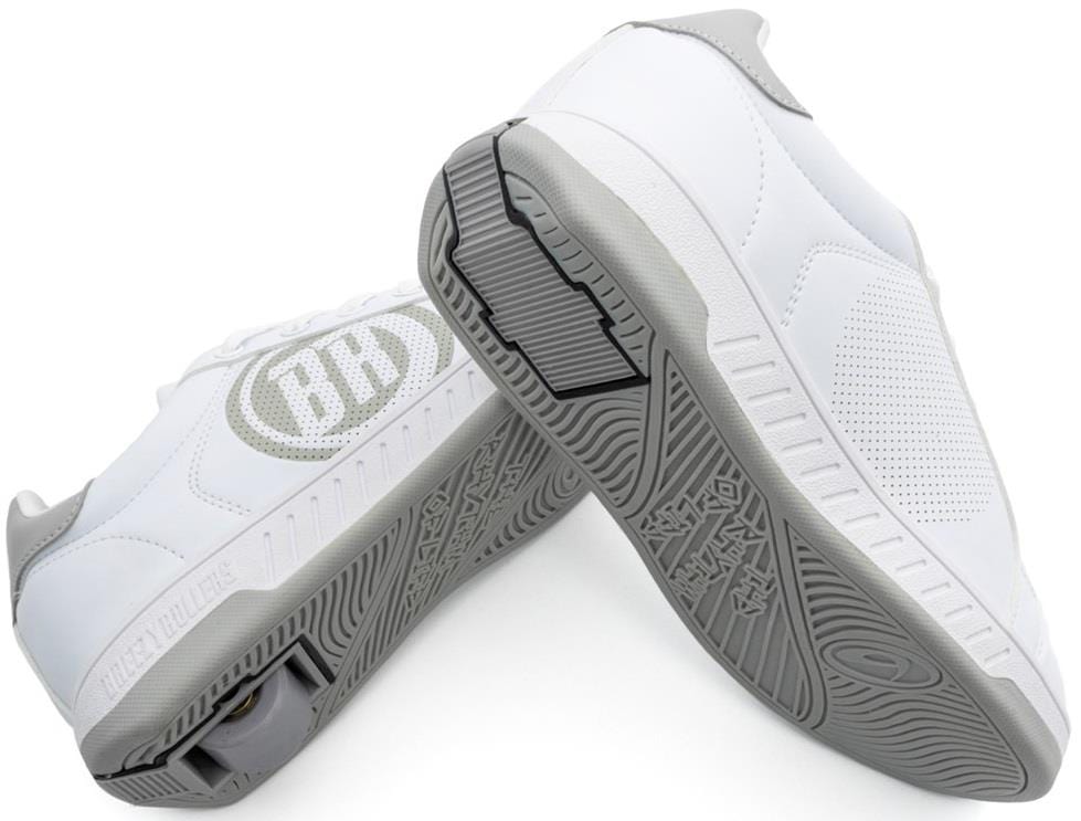A pair of Breezy Rollers Classic Shoes - White / Grey by Breezy Rollers: one stands upright, displaying the patented wheel system in the sole, while the other tilts to reveal a side logo and perforated details.