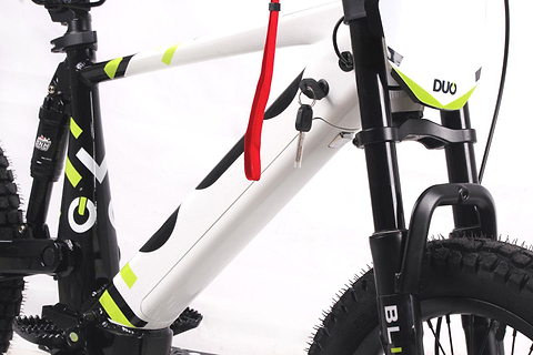 Close-up of the Duo 18" Blitz Kids Electric Balance Bike in white/black, highlighting the battery compartment with key and red strap, plus visible front suspension fork and part of the tires.