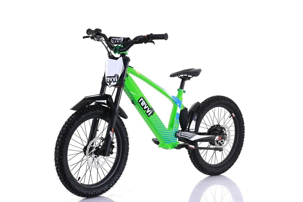 The Revvi 20" Kids Electric Balance Bike - Green showcases a vivid green frame with black wheels and seat, featuring off-road tires, front suspension, and disc brakes. "Revvi" branding is prominent on the frame and handlebars. It's displayed on a reflective white surface.
