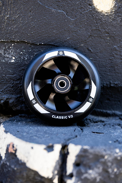 A Union Classic V2 110mm Stunt Scooter Wheel in black with a visible metal bearing leans against a rough, chipped black-and-white painted stone surface.