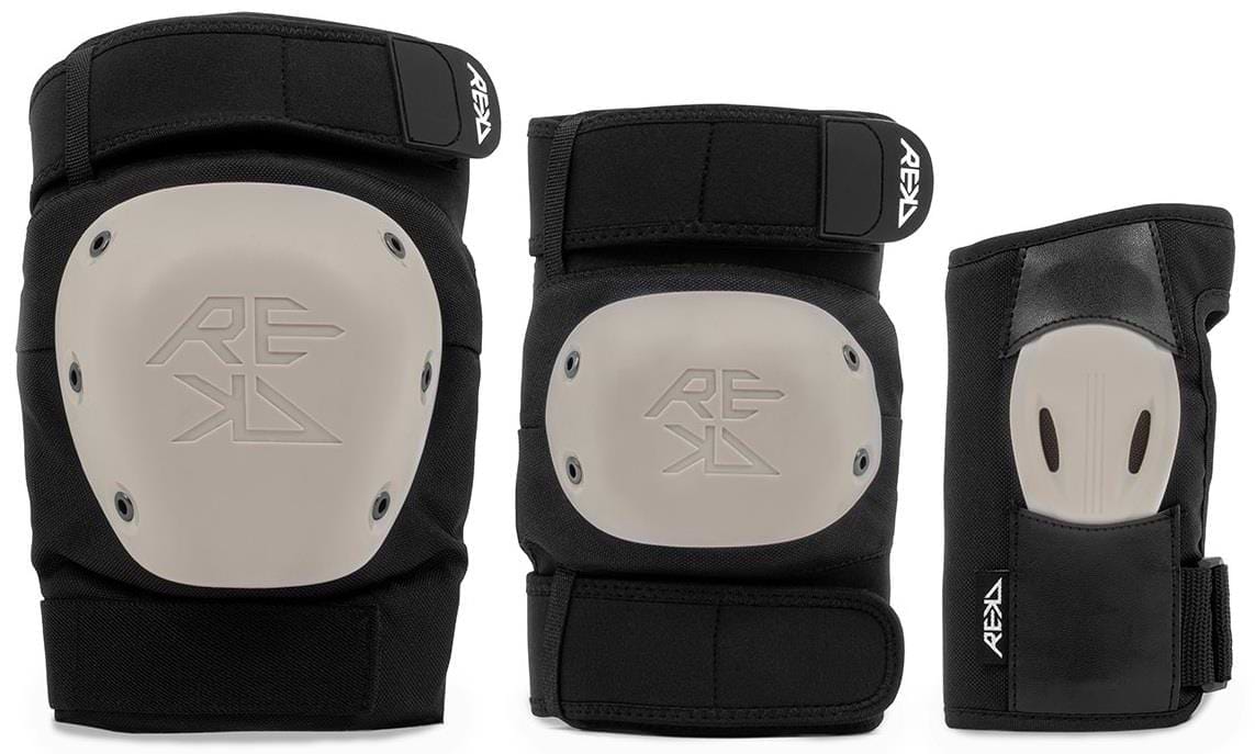 The REKD Shield Triple Skate Protection Pad Set in Black/Beige includes a knee pad and elbow pad with beige hard shells, plus a wrist guard with a high-impact palm splint—all offering premium action sports protection and featuring the REKD logo.