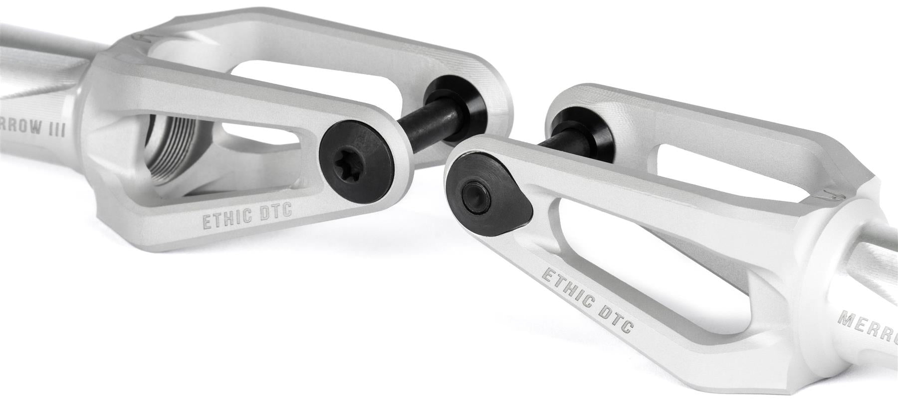 Close-up of two Ethic DTC Merrow V3 8/12STD HIC Stunt Scooter Forks in Raw by Ethic, featuring black bolts and angular design, engraved "ETHIC DTC," displayed against a white background.