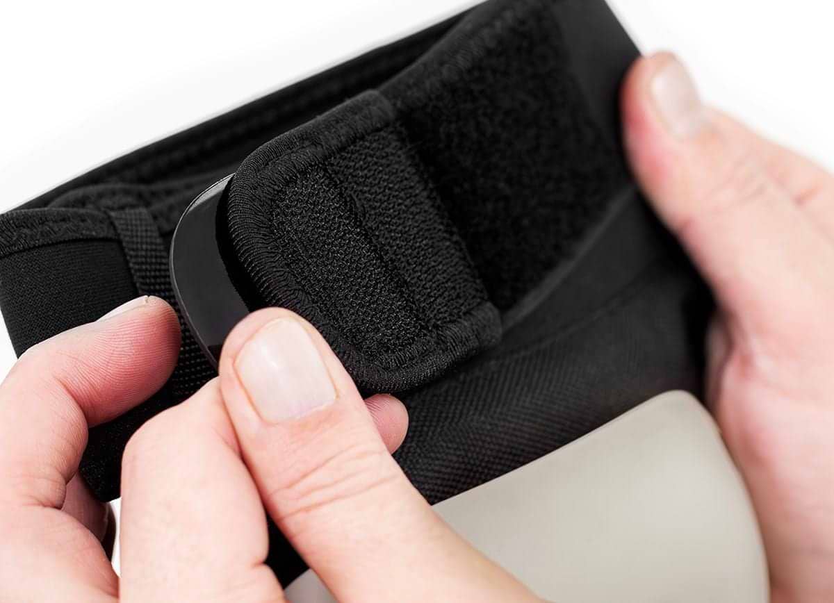 Close-up of two hands adjusting a black Velcro strap on REKD Shield Triple Skate Protection Pad Set by REKD, against a white background.