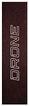 Close-up of the Drone Prism Glitter Stunt Scooter Griptape - Red, featuring bold white letters vertically aligned on a dark, speckled background. The texture resembles fine silica grit for enhanced traction and style.