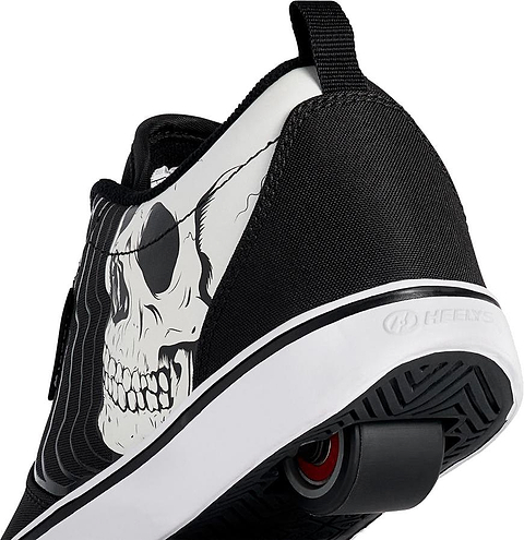 A close-up of the Heelys Pro 20 PRNT Glow Boys Shoes by Heelys in black/white, showing a glow-in-the-dark skull graphic on the side and low-profile wheels in the sole for smooth rolling.