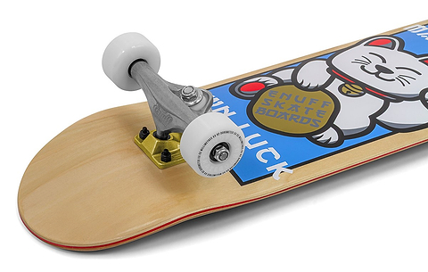 A close-up of the Enuff Lucky Cat Natural Complete Skateboard (8.0" x 32")—a beginner board with white wheels, wooden deck, and a blue design featuring a waving lucky cat and "ENUFF SKATE BOARDS" and "GOOD LUCK" text.