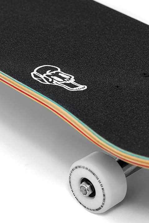 Close-up of the Enuff Yokai Dragon Complete Skateboard - 8.25" x 32.1", featuring black grip tape, a white skull graphic on a multicolored maple deck, and a white wheel with metal axle. Brand: Enuff.