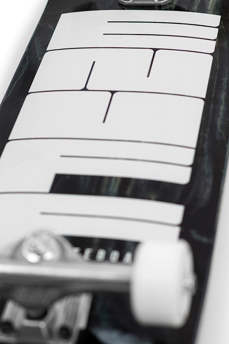 Close-up of the Enuff Throwback Black Complete Skateboard (8.5" x 32.1") deck, featuring a bold abstract white graphic on 7-ply maple, plus a metallic front truck and white wheel for that classic retro Enuff vibe.