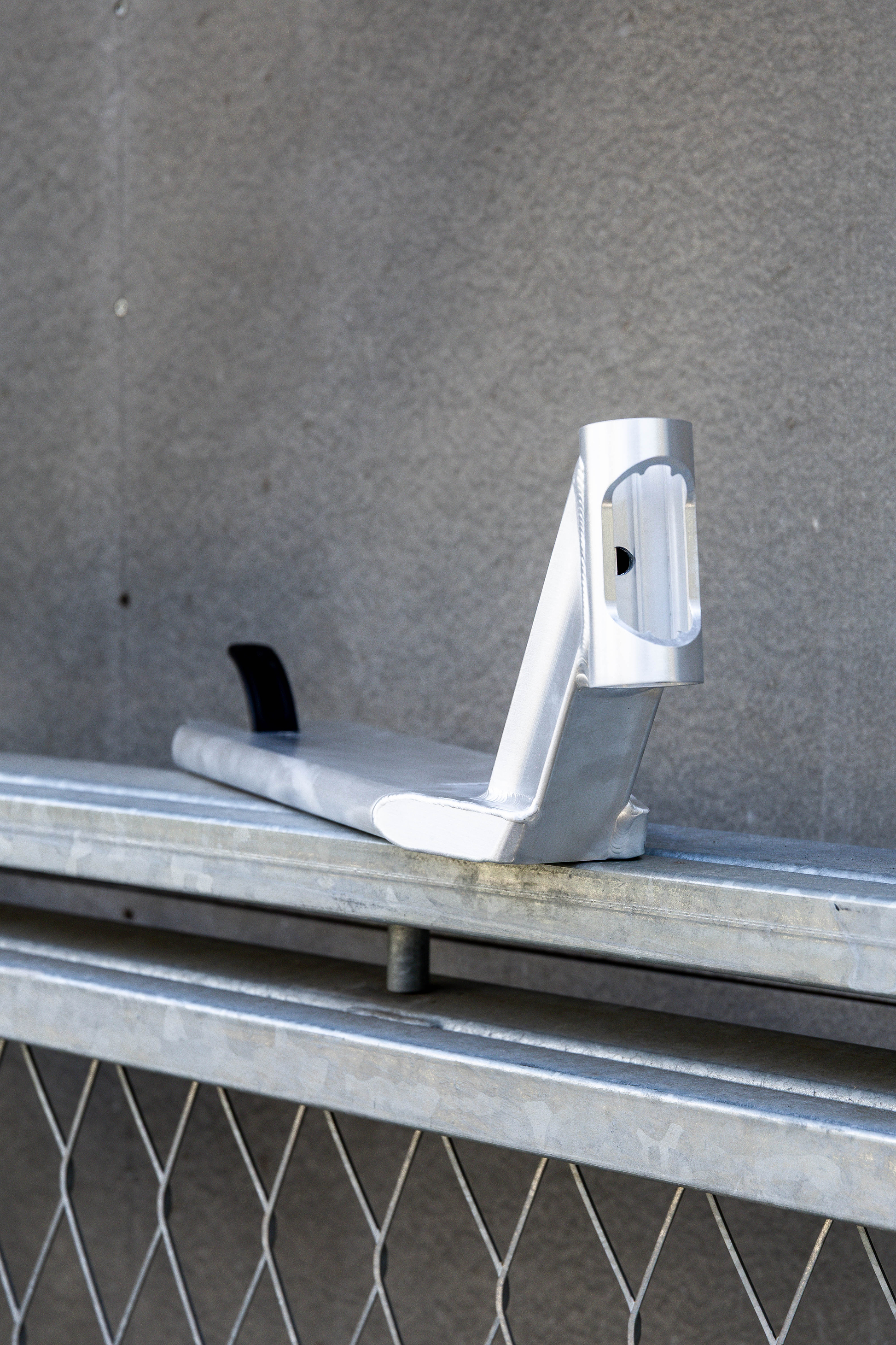The Union Classic Pro Silver Stunt Scooter Deck - 4.75" by Union features a sturdy silver metal bracket with a curved base, upright section, black insert, and rectangular cutout, mounted on a galvanized bar against a gray wall.