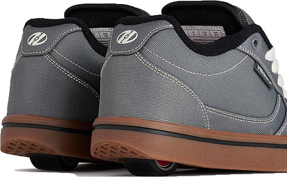 A close-up of the Heelys Pro 25 Boys Shoes in Grey, Antique White, and Black showcases their stylish gum soles and concealed wheels in the heels. Designed by Heelys, these sneakers provide both walking comfort and rolling fun with two wheels per shoe for added stability.