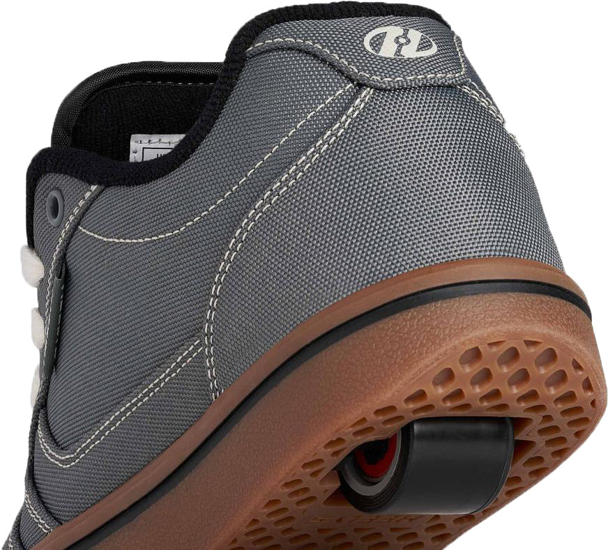 Close-up of the back of a gray sneaker with white stitching and a brown sole, featuring a retractable wheel in the heel—perfectly showcasing the Heelys Pro 25 Boys Shoes in Grey / Antique White / Black by Heelys.
