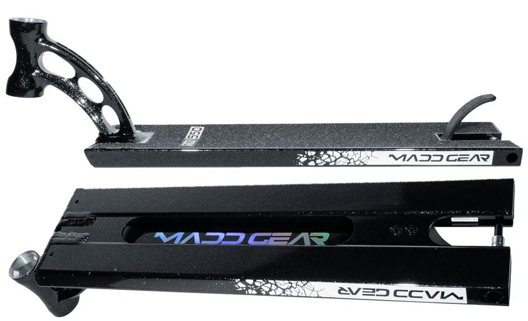Two Madd Gear MGP VX Origin Black Stunt Scooter Decks (5.5″ x 20.5″) are displayed—one upright revealing its grip tape and foot brake, while the other is flipped to showcase the underside featuring a holographic logo and distinctive white crackle design—an ideal choice for park riders seeking standout style from Madd Gear.