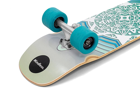 A close-up of the Mindless Drifter Cruiser Skateboard 28″ x 8″ - Teal shows teal wheels, silver trucks, and geometric teal and white designs, with “Mindless” on a black circle at the tail.