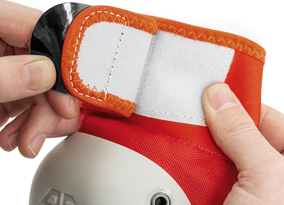 Close-up of hands fastening a red and white Velcro strap on the REKD Shield Triple Skate Protection Pad Set in Fade Orange / Green by REKD.