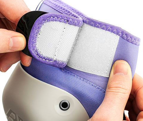 Two hands fastening the Velcro strap of a light purple and gray protective knee pad from the REKD Shield Triple Skate Protection Pad Set - Fade Red / Violet by REKD, which includes matching wrist guards for comprehensive action sport protection.