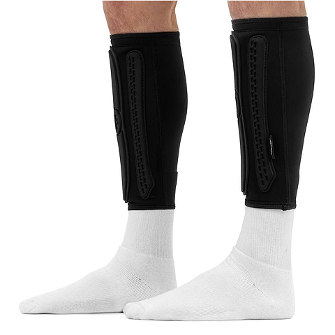 Slim black REKD Energy Covert Long Shin Skate Protection Guards worn over white socks on a person’s lower legs.