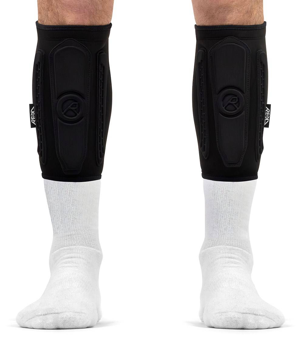Black REKD Energy Covert Short Shin Skate Protection Guards worn for impact protection over white socks on a person’s lower legs.