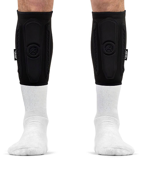 Black REKD Energy Covert Short Shin Skate Protection Guards worn for impact protection over white socks on a person’s lower legs.