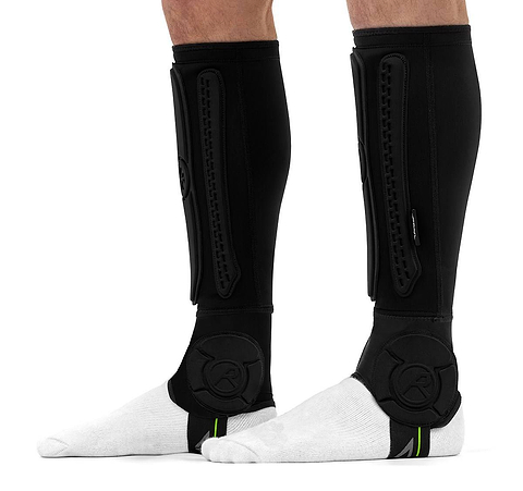 Black REKD Energy Covert Long Shin and Ankle Skate Protection Guards worn over white socks, featuring protective padded panels on the shins and sides of the ankles for BMX ankle protection.