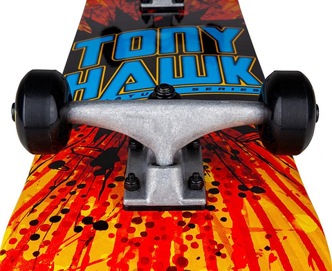 Close-up of the Tony Hawk SS 180 Series Shatter Logo Complete Skateboard—featuring bold blue “Tony Hawk” text and a vivid red-and-yellow shatter design on its 7.75″ x 31″ maple deck—showing off the front trucks and black wheels; perfect as a beginner complete skateboard.