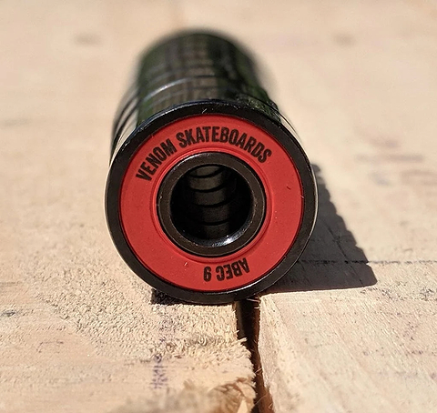 Close-up of a cylindrical Venom ABEC 9 Skateboard Bearings - 8 Pack with a red rim printed with the text “VENOM SKATEBOARDS” and “ABEC 9”.