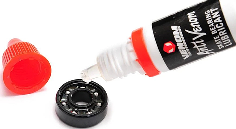 A Venom AntiVenom Bearing Lube 10ml bottle applying a drop of clear liquid into a black skateboard bearing.