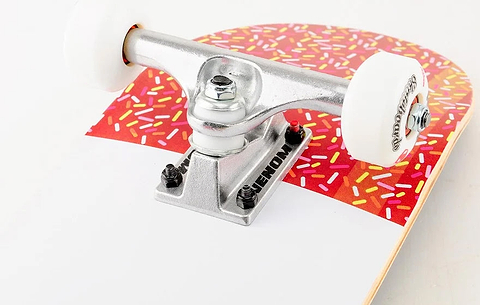 Close-up of a Venom Junior Ice Lolly Kids Complete Skateboard - 7.25″ x 29″ with white wheels, showing the deck decorated with a red pattern of colorful sprinkles.