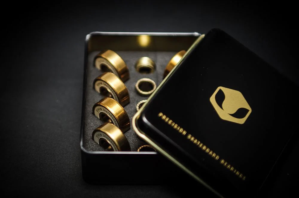 Eight gold-colored Venom Precision Gold Skateboard Bearings stored in a black metal tin with a matching lid.
