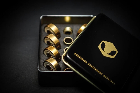 Eight gold-colored Venom Precision Gold Skateboard Bearings stored in a black metal tin with a matching lid.