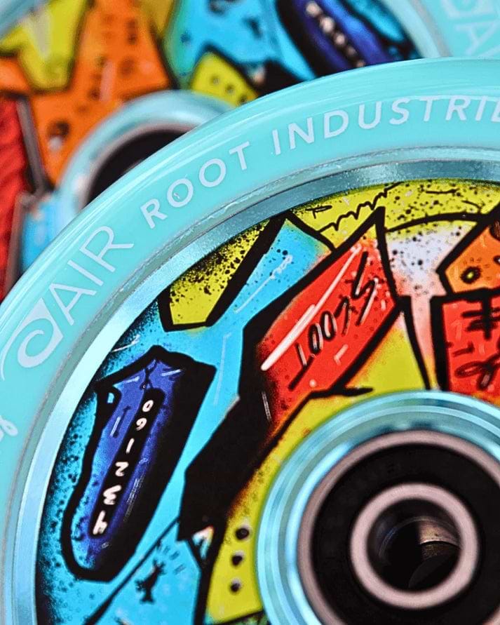 Close-up of two colorful Root Industries x KOTA Limited Edition AIR 110mm Stunt Scooter Wheels in blue, featuring abstract graffiti-inspired designs and visible ball bearings, with "AIR ROOT INDUSTRIES" printed on the rim.