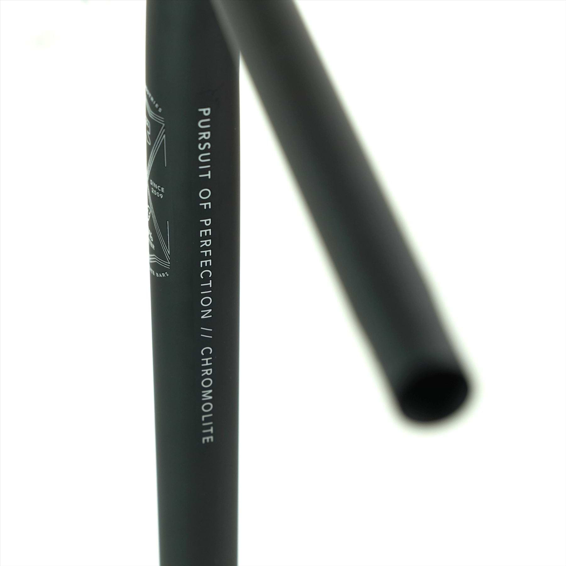 A close-up of the black Root Industries ChromoLite Steel Oversized HIC Stunt Scooter T-Bars reveals white text stating "PURSUIT OF PERFECTION // CHROMOLITE." These sleek bars, measuring 620mm x 600mm, stand out against a blurred background, showcasing their refined design resembling premium stunt scooter bars.
