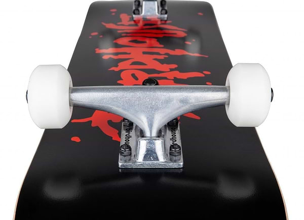Close-up of a Birdhouse Stage 1 Blood Logo Black Complete Skateboard measuring 8" x 31.5", highlighting its silver trucks, white wheels, and black deck adorned with red graffiti-style writing. The emphasis is on the skateboard's hardware and vibrant design, making it ideal for beginner-friendly skating.