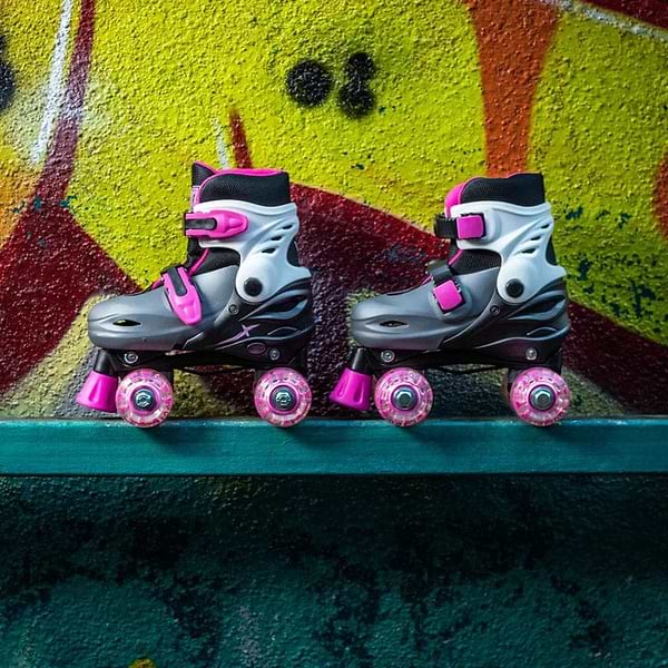 A pair of Xootz LED Adjustable Quad Roller Skates in pink rest side by side on a teal ledge, set against a vibrant graffiti-covered wall.