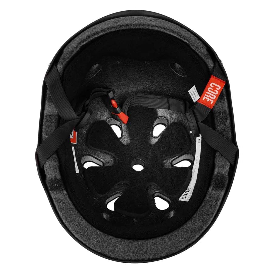 The image showcases the interior of a CORE Street Skate / Scooter Helmet in Stealth Black. This helmet includes Lux Pads for enhanced comfort and style, along with ventilation holes. It features black straps accented with red and white tags, contributing to its simple yet functional design.
