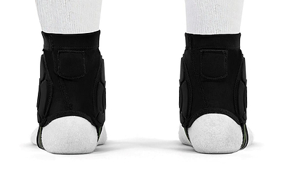 A rear view of two feet wearing white socks and REKD Energy Covert Ankle Impact Skate Protection Guards - Black by REKD, featuring energy-absorbing protection, standing side by side on a white surface.