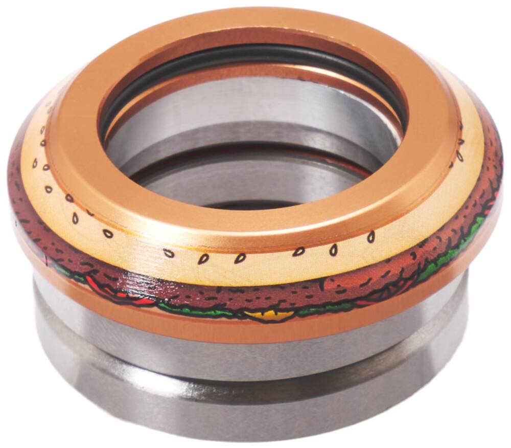 The image shows a detailed view of a metallic object that resembles the Chubby Integrated Stunt Scooter Headset - Burger Boy. It features a colorful design akin to a hamburger with buns, lettuce, tomato, and beef patty. The sealed bearing in the photo could seamlessly be part of a stunt scooter headset. The background is white.