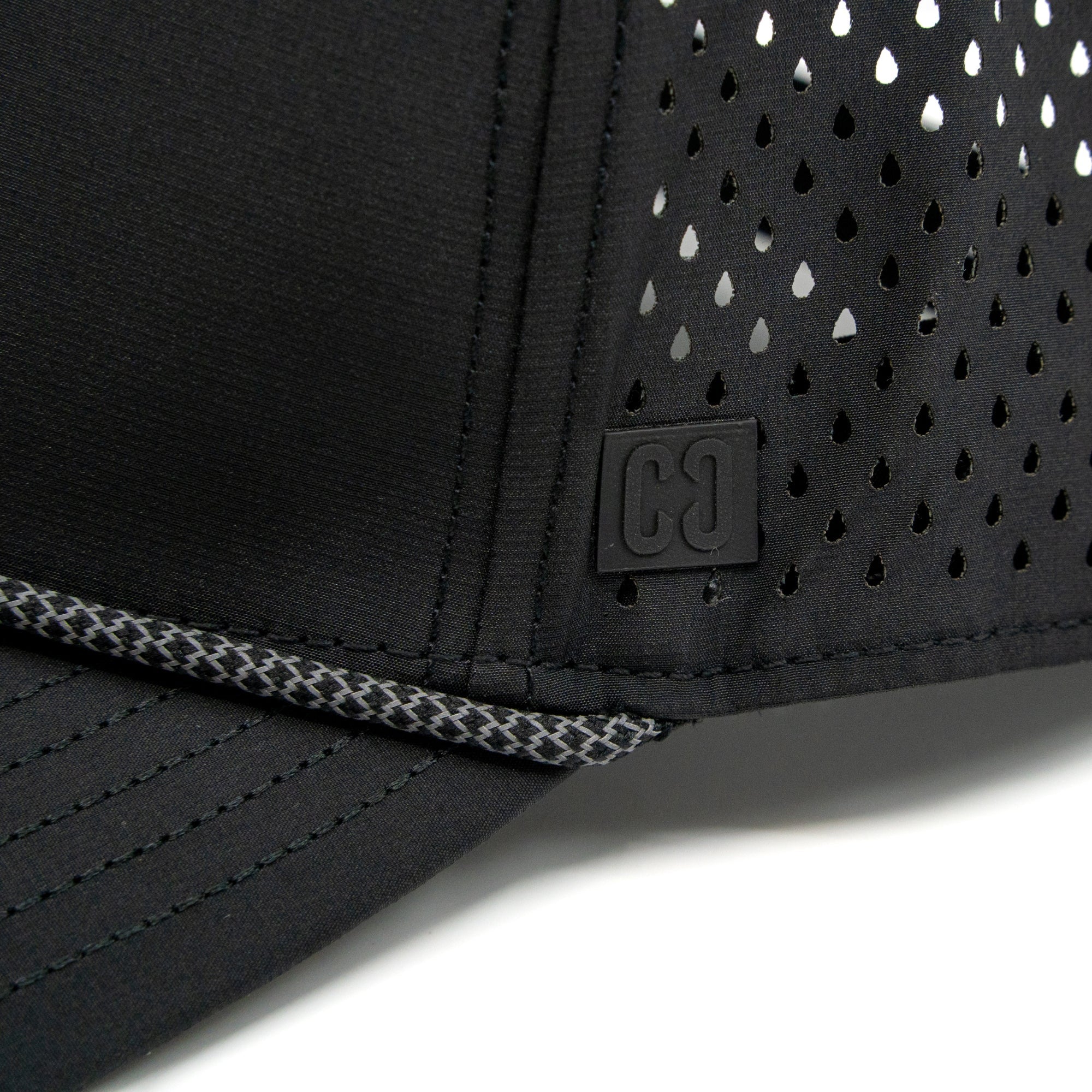 Close-up of the CORE Aero Rope Cap in black, featuring ventilated holes, prominent stitching, and a small square CORE logo patch with “C C” on the front near the brim.